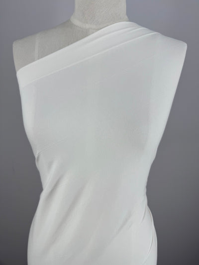 A white dress made of Super Cheap Fabrics' Cotton Lycra - Sugar Swizzle (135cm) is showcased on a mannequin against a gray background. The stretchy, medium-weight material gently hugs the body, enhancing its elegant silhouette.
