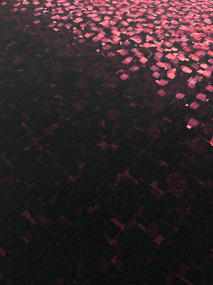 A close-up of the Super Cheap Fabrics Designer Lycra Panel (90cm) shows a dark surface with small, glowing pink and red squares forming a dense, bright pixelated pattern across its entire length and width.