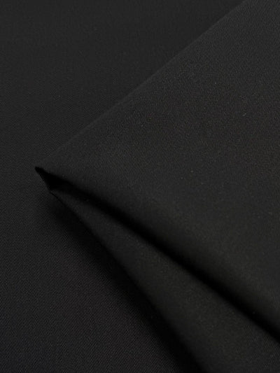 The Gabardine - Black - 150cm by Super Cheap Fabrics showcases a smooth texture with fine diagonal twill lines. Draped into a neat, gentle pointed fold, the durable and slightly reflective fabric gives off an elegant appearance.