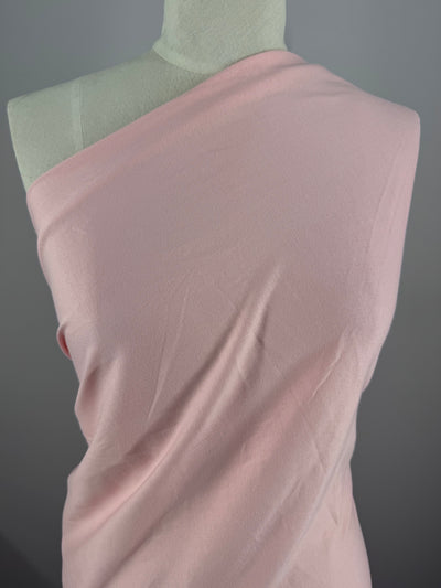 A Super Cheap Fabrics mannequin is draped in Cotton Jersey - Tickled Pink - 170cm fabric, elegantly wrapped over one shoulder. The neutral gray background enhances the texture and color of this stylish display.