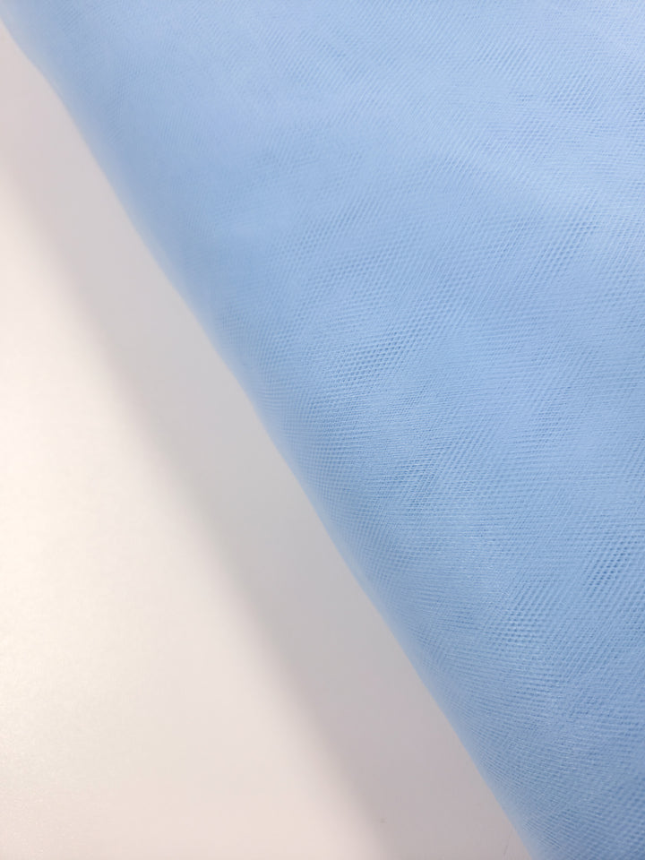 A close-up of Super Cheap Fabrics' Soft Tulle - Spun Sugar (150cm) in light blue, featuring a subtle textured pattern draped over white—ideal for bridal veils or elegant crafts.