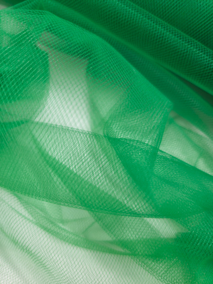 Close-up of Super Cheap Fabrics' Soft Tulle - Emerald (150cm), a lightweight, semi-transparent green fabric with a fine grid pattern. Drapes softly, allowing light through for subtle shadows and layered effects.