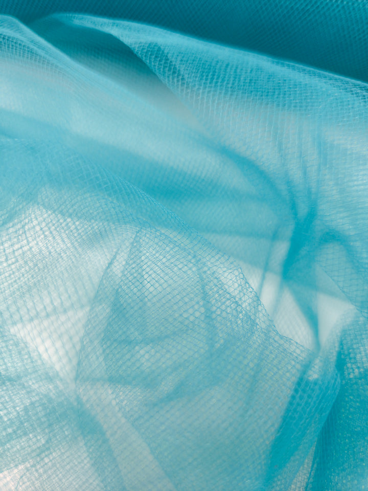 A close-up of Super Cheap Fabrics' Soft Tulle - Lake Blue - 150cm shows its delicate, fine mesh texture, softly layered and folded—ideal for bridal veils or crafts, this airy fabric lets light through for a dreamy effect.