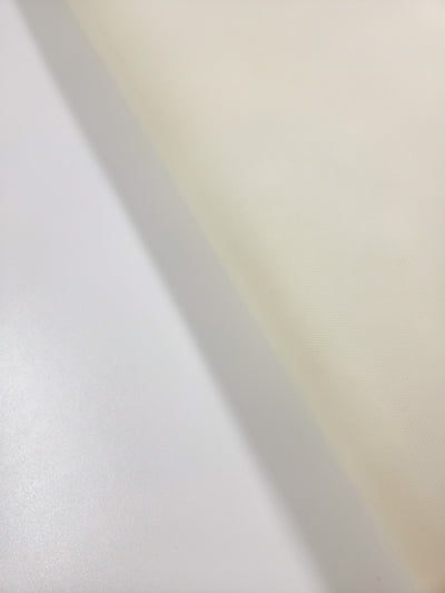A close-up of a surface with a diagonal divide: smooth white on the left, and slightly textured cream on the right, evoking the delicate contrast found in Super Cheap Fabrics' Soft Tulle - Cream - 150cm, ideal for bridal veils.