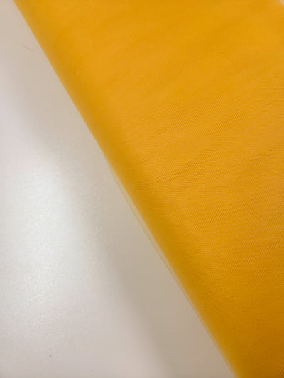 A close-up of Super Cheap Fabrics’ Soft Tulle - Yellow - 150cm, a sheer, lightweight fabric ideal for veils, shown folded on a smooth white surface.