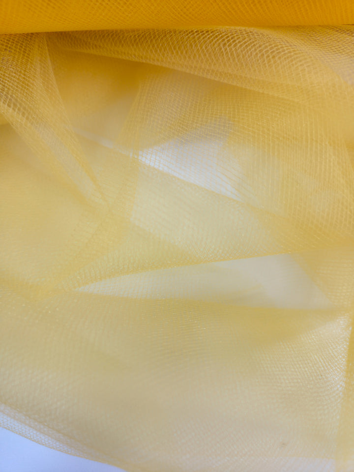 A close-up of Super Cheap Fabrics’ Soft Tulle - Yellow - 150cm displays its delicate, translucent texture and soft folds in lightweight sheer fabric, ideal for bridal veils.