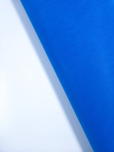 The Super Cheap Fabrics Soft Tulle - Royal - 150cm roll is displayed diagonally on a white background, with vibrant blue material stretching from top right to bottom left—ideal for crafts or bridal veils.