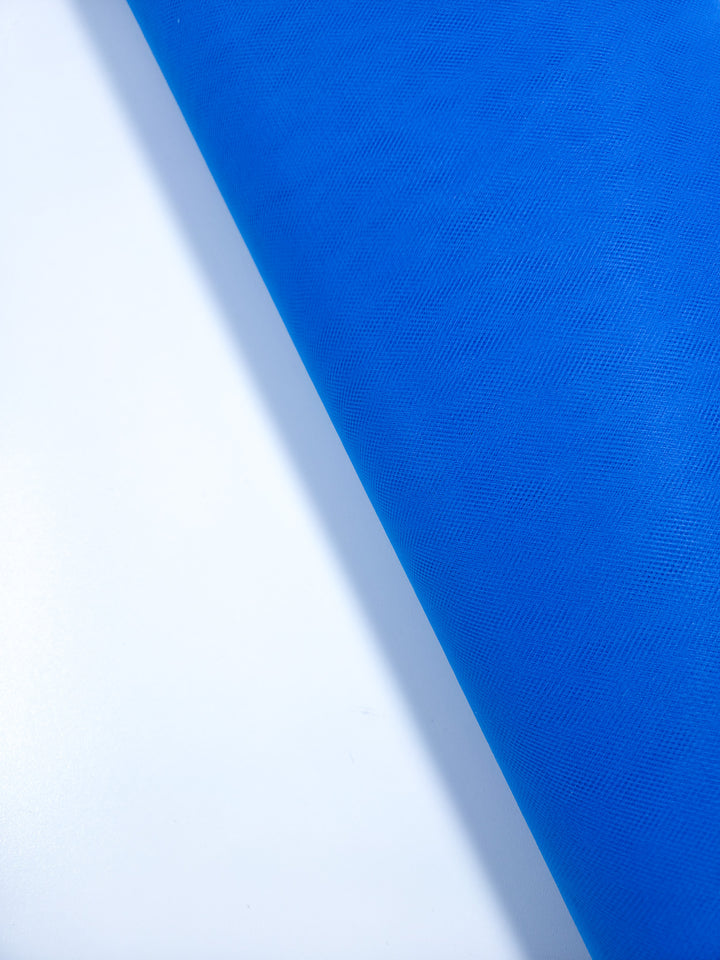 The Super Cheap Fabrics Soft Tulle - Royal - 150cm roll is displayed diagonally on a white background, with vibrant blue material stretching from top right to bottom left—ideal for crafts or bridal veils.