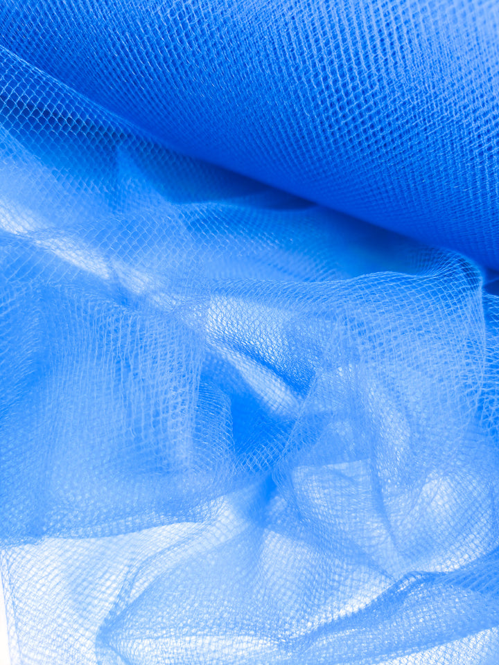 Close-up of Super Cheap Fabrics’ Soft Tulle - Royal - 150cm reveals its delicate, sheer net texture—ideal for bridal veils or crafts—as light filters through the bright blue mesh and gentle folds.