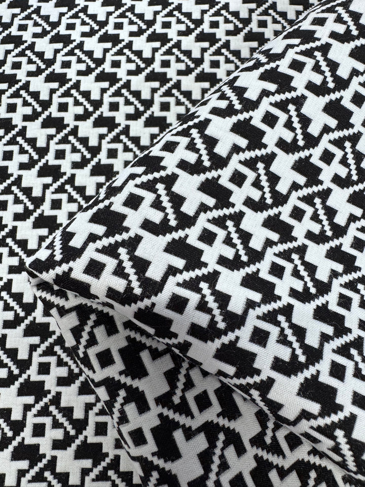 Designer - Brushstrokes - Black & White by Super Cheap Fabrics is a 148cm wide, 100% polyester fabric featuring a bold, geometric zigzag pattern with interconnected diamond and cross shapes. Two pieces are shown folded to display the repeating design.