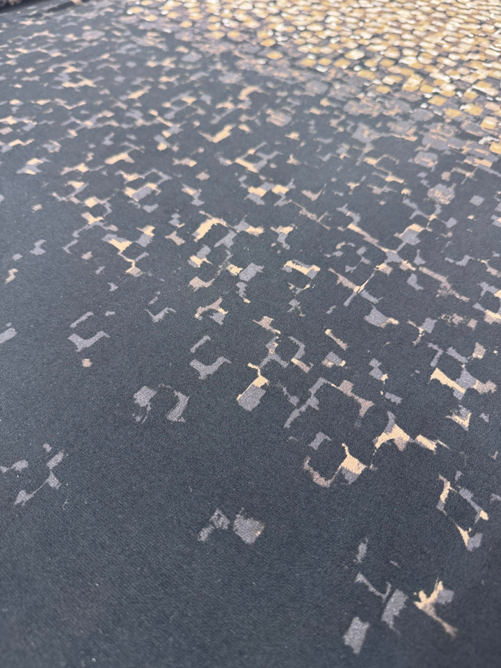 Close-up of Super Cheap Fabrics' Designer Lycra Panel – 90cm Panel, featuring dark fabric with small, irregular gold and beige geometric shapes for a textured, abstract look. Perfect for projects needing custom widths or panel lengths.
