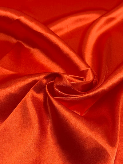 Super Cheap Fabrics’ Satin Back Crepe - Orange - 150cm features a glossy, smooth finish with gentle folds that reflect light, making it ideal for elegant eveningwear and adding a touch of sophistication.