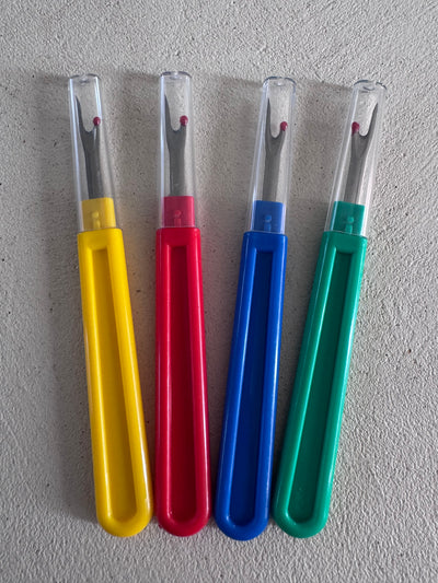 Four Super Cheap Fabrics Unpicker seam rippers with plastic handles in yellow, red, blue, and green—each with a clear cap—are arranged side by side on a light textured surface, perfect for precise stitch removal.