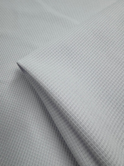 A close-up of Super Cheap Fabrics' Waffle Knit - White - 170cm reveals a soft, white waffle weave with a subtle grid pattern and folded layers, highlighting the texture of this unique knit fabric.