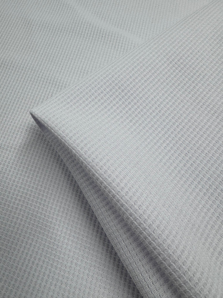 A close-up of Super Cheap Fabrics' Waffle Knit - White - 170cm reveals a soft, white waffle weave with a subtle grid pattern and folded layers, highlighting the texture of this unique knit fabric.