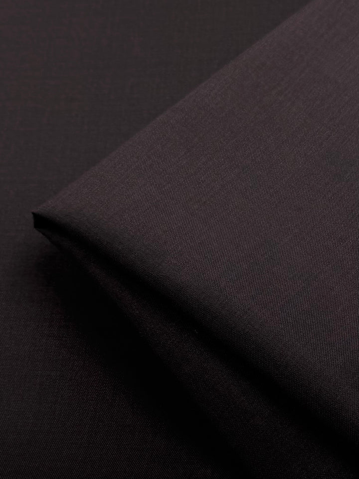 A close-up of neatly folded Super Cheap Fabrics Twill Suiting in chocolate (150cm), featuring a smooth, slightly textured surface with clean lines and subtle lighting.