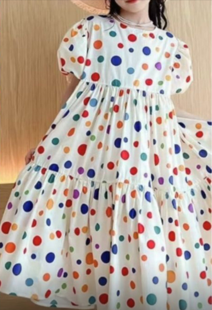 A person in a tiered white dress with puffed sleeves and flared skirt, made from Super Cheap Fabrics' Designer Rayon - Pop of Colour (145cm), featuring vibrant multicolored polka dot prints and a gathered waist.