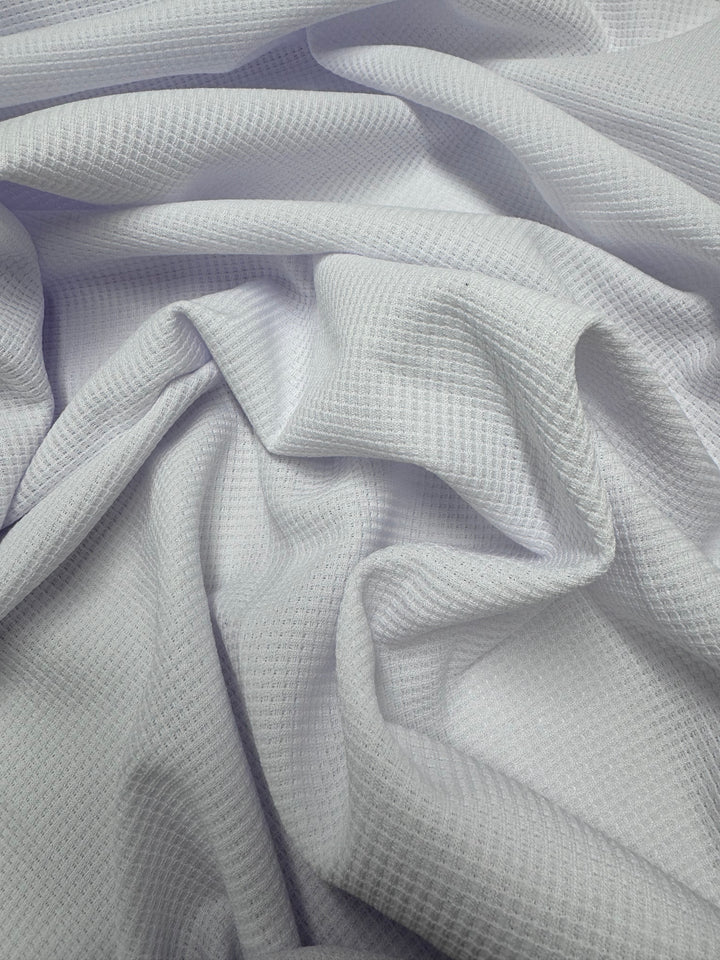 Close-up of Super Cheap Fabrics' Waffle Knit - White - 170cm, highlighting its light color, textured grid pattern, and soft draped creases.