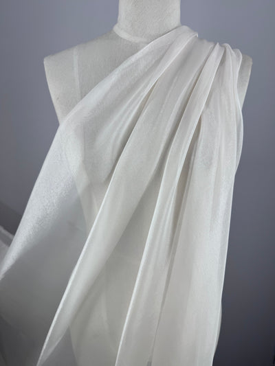 A white dress form is draped in Blended Silk Mousseline - Bridal Blush by Super Cheap Fabrics, styled like a classic toga. The sheer fabric elegantly cascades over the shoulder, evoking a bridal blush against the neutral gray background.