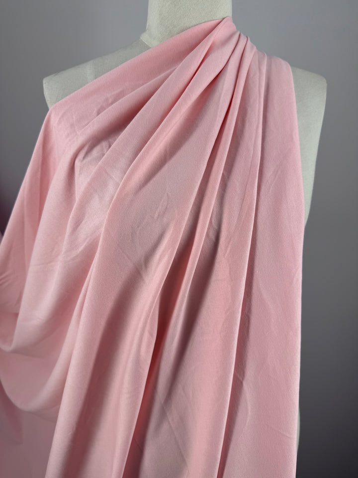 The Cotton Jersey - Tickled Pink fabric by Super Cheap Fabrics, measuring 170cm, elegantly drapes over a mannequin with gentle folds and a smooth texture. A neutral gray background accentuates the fabric's color and texture.