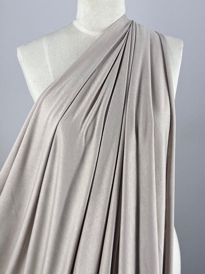 A close-up of a mannequin draped in Super Cheap Fabrics' Cotton Jersey - Oatmeal (150cm), arranged diagonally from the left shoulder, showing the fabric’s gentle folds and smooth, flowing lightweight texture.
