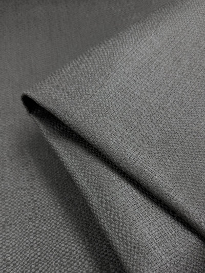 A close-up of Dorian Upholstery - Gunmetal (146cm) by Super Cheap Fabrics shows soft, textured grey fabric with a subtle woven pattern—ideal for high-end upholstery projects.