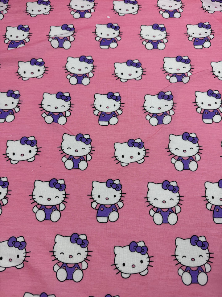 The "Printed Jersey - Kitty - 162cm" by Super Cheap Fabrics features adorable cartoon cats with bow-adorned ears and overalls, set on a pink backdrop. This Poly/Cotton blend ensures a lightweight feel with neatly aligned cat images for a playful yet elegant touch.