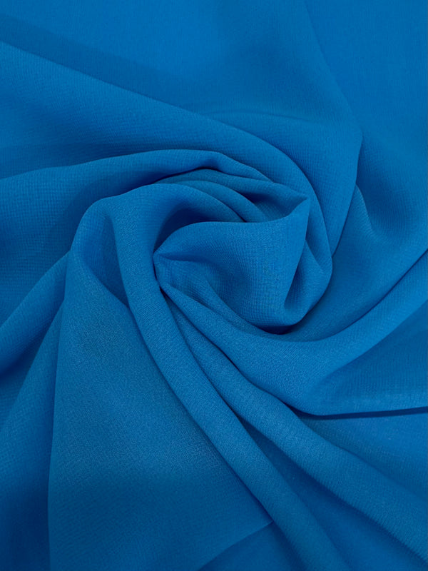 A close-up of Super Cheap Fabrics' Hi-Multi Chiffon - Vivid Blue (148cm) shows vibrant blue polyester arranged in soft, swirling folds with a textured, flowing pattern.
