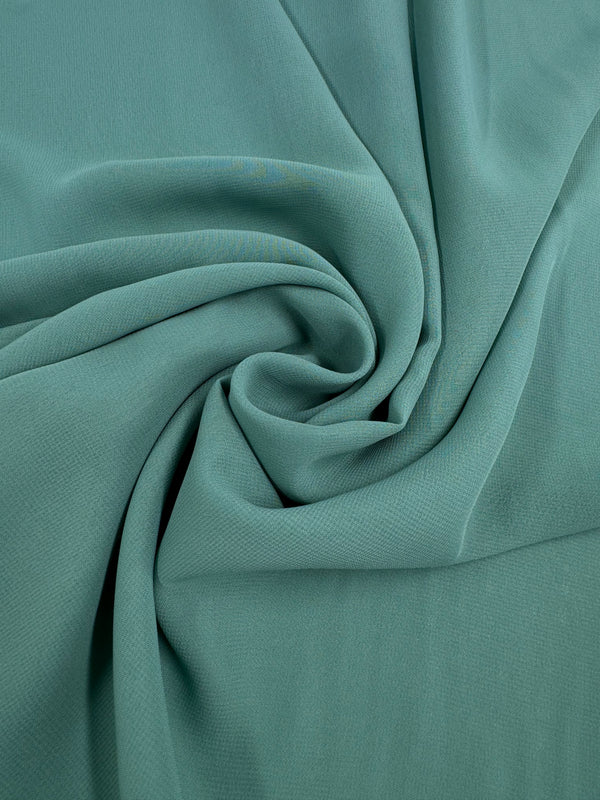 A close-up of Super Cheap Fabrics' Hi-Multi Chiffon in Basil (148cm), light teal sheer fabric elegantly draped and gathered into a swirl, showcasing natural folds and delicate texture.
