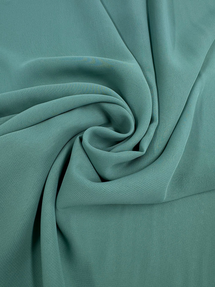 A close-up of Super Cheap Fabrics' Hi-Multi Chiffon in Basil (148cm), light teal sheer fabric elegantly draped and gathered into a swirl, showcasing natural folds and delicate texture.