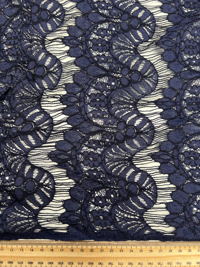 Evening Lace - Crown Of Navy - 135cm by Super Cheap Fabrics features intricate navy blue floral lace on a light background, displayed next to a 40cm ruler for scale. This lightweight fabric blends elegance with detailed patterns.