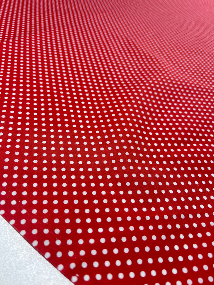 A close-up of Super Cheap Fabrics' "Cotton Dots Mini - Red - 112cm" shows a red printed cotton with evenly spaced white dots forming a gradient: denser and larger in the foreground, becoming smaller and less dense towards the background.