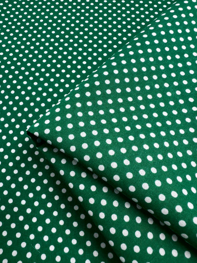 Lightweight Cotton Dots Mini - Emerald fabric, from Super Cheap Fabrics, offers a blend of natural cotton fibers with white polka dots. At 112cm wide, it provides a soft and breezy touch; slightly folded at the corner for easy handling.