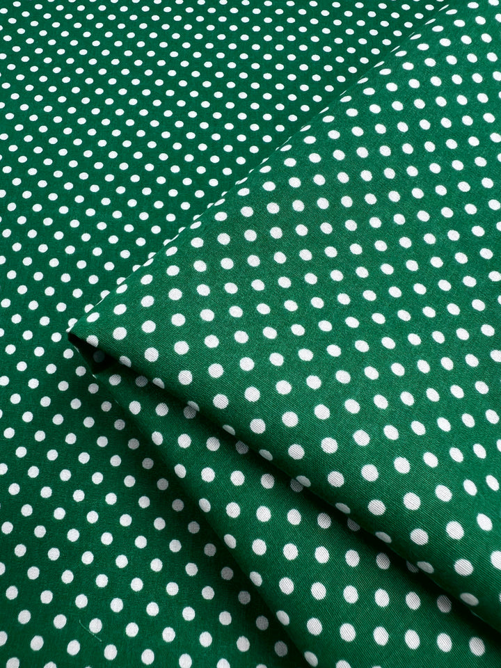Lightweight Cotton Dots Mini - Emerald fabric, from Super Cheap Fabrics, offers a blend of natural cotton fibers with white polka dots. At 112cm wide, it provides a soft and breezy touch; slightly folded at the corner for easy handling.