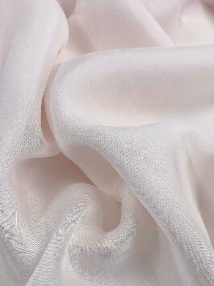 A close-up of the Pure Silk Chiffon - Bridal Blush from Super Cheap Fabrics showcases its soft, white fabric with gentle folds and smooth texture, creating a serene and elegant appearance. This 140cm extra lightweight fabric appears slightly translucent, evoking a sense of bridal blush.