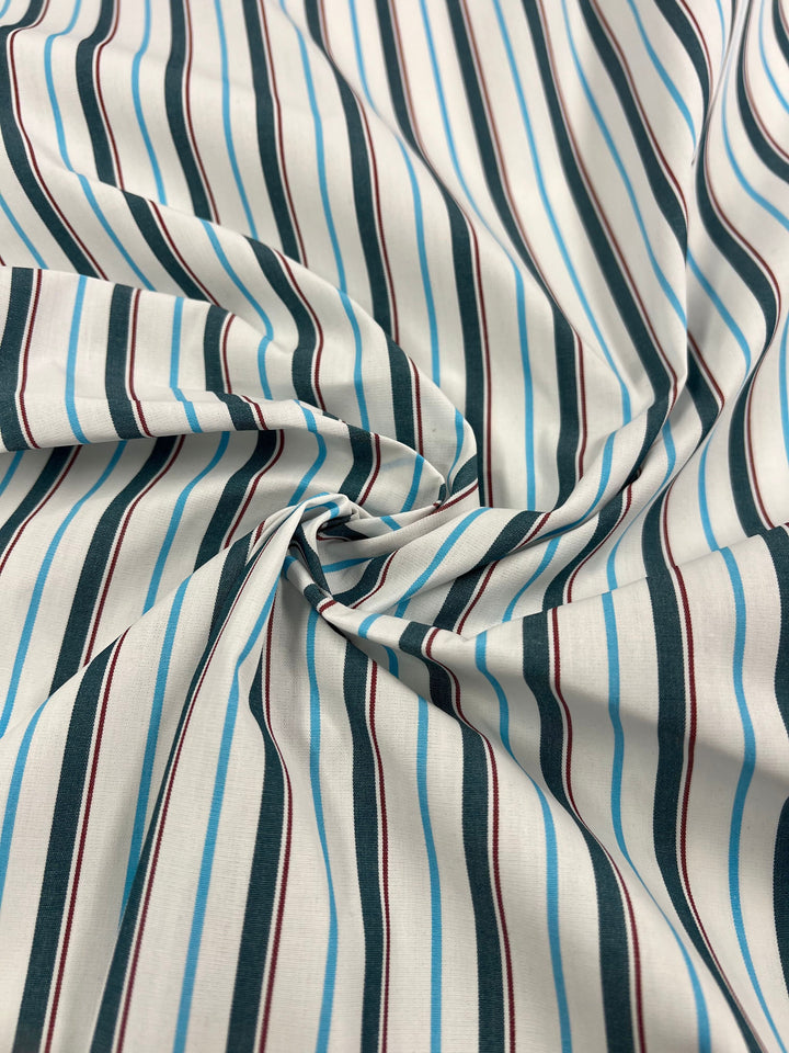 A close-up of Shirting - Marquee - 150cm by Super Cheap Fabrics, a lightweight polyester cotton blend with vertical black, light blue, and red stripes twisted at the center—perfect for dresses.