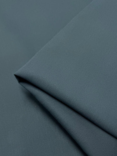 A close-up of Super Cheap Fabrics' Gabardine - Cilantro - 150cm highlights the neatly folded, wrinkle-resistant dark green fabric's smooth texture and subtle sheen with layered, visible edges for a clean look.