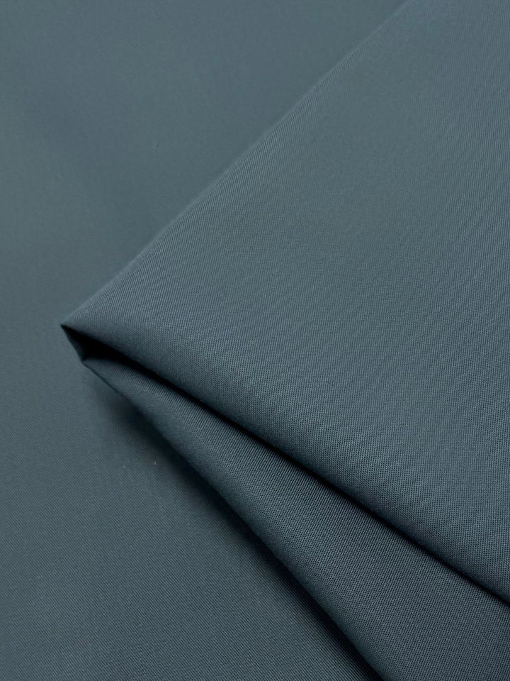A close-up of Super Cheap Fabrics' Gabardine - Cilantro - 150cm highlights the neatly folded, wrinkle-resistant dark green fabric's smooth texture and subtle sheen with layered, visible edges for a clean look.