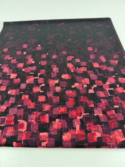 The Super Cheap Fabrics Designer Lycra Panel features red and pink squares in various shades on a dark background. Available as a 90cm panel, this versatile fabric is displayed on a white surface and suits many project needs.