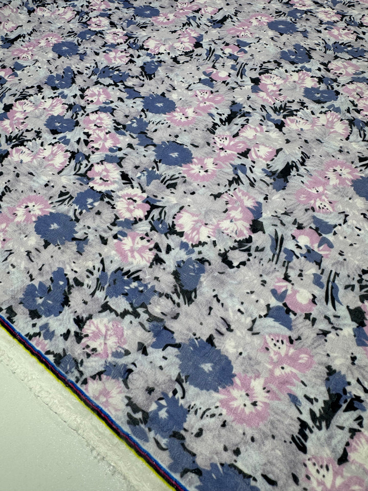 The Designer Jacquard - romi by Super Cheap Fabrics features a lightweight floral pattern with pink, blue, and black flowers on light gray. Edges display layers of hues, underscoring its versatility as a multi-use fabric. Width: 145cm.