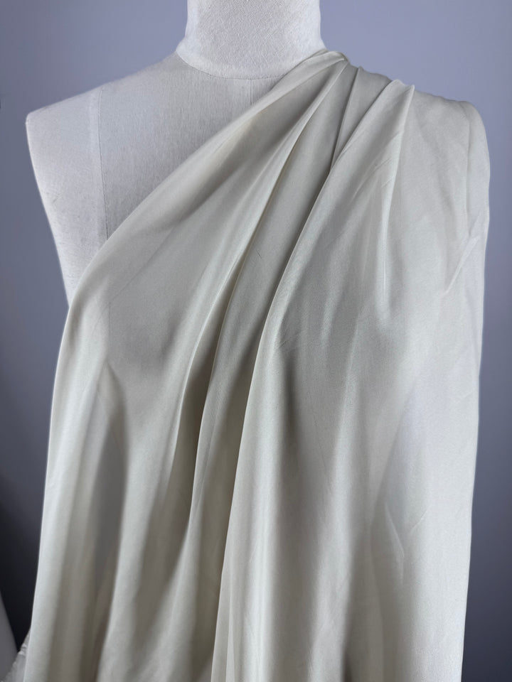Super Cheap Fabrics’ Pure Silk Chiffon - Oyster (140cm) is draped elegantly on a white dress form, showcasing its lightweight, soft folds—perfect for summer outfits—against a light gray background.