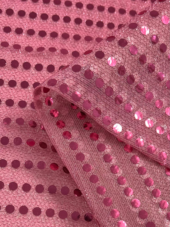 Super Cheap Fabrics' Sequin - Pink - 112cm is a mesh fabric adorned with shiny pink sequins, folded to highlight its sparkle and flexibility—ideal for standout costumes or dancewear.