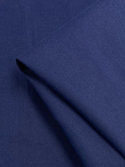 A close-up of folded Drill - Navy Peony - 150cm fabric by Super Cheap Fabrics, showing a smooth, slightly textured surface. The medium weight fabric is neatly creased and has a clean, uniform appearance, indicating high-quality material suitable for clothing or upholstery.