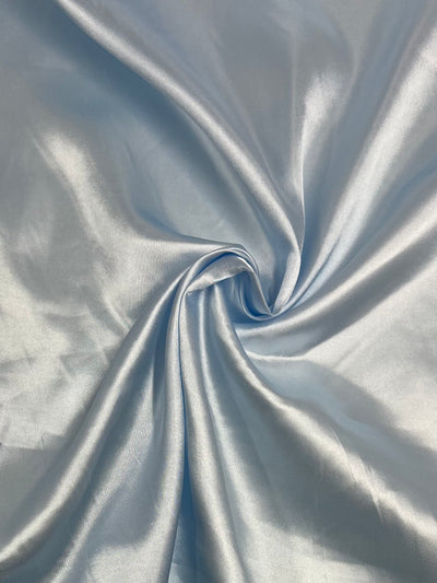 Super Cheap Fabrics’ Satin - Ice - 150cm: shiny light blue satin with a smooth texture, softly gathered at the center for elegant folds and a subtle swirl—ideal for chic dresses or stylish home décor.