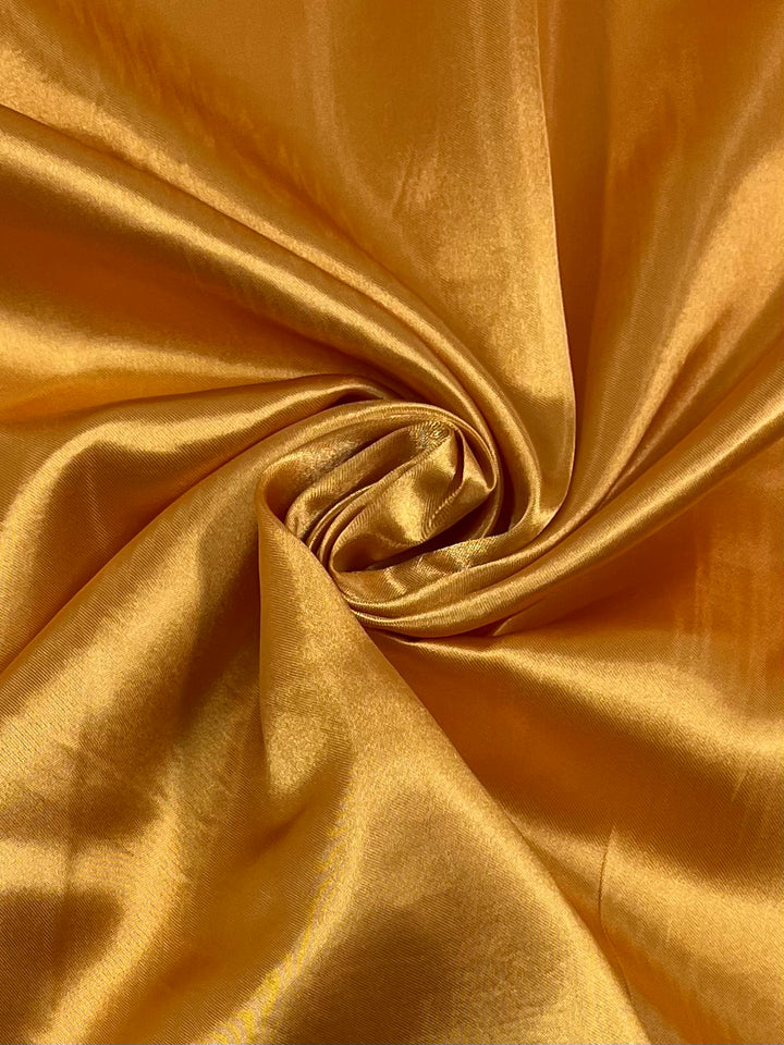 Super Cheap Fabrics' Satin - Gold - 150cm features lustrous golden-yellow fabric with a smooth, shiny texture and soft drape—ideal for luxurious dressmaking projects.