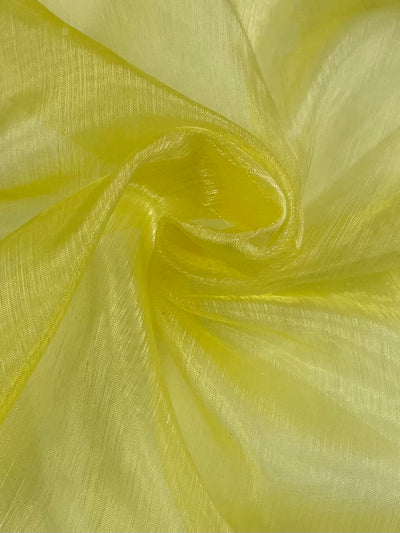 A close-up of Super Cheap Fabrics’ Organza - Yellow - 150cm, showcasing its light yellow, slightly shimmery texture gently folded to form soft, flowing curves.