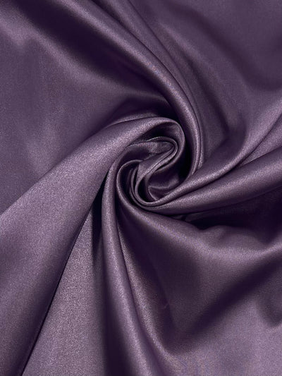 A close-up of Satin - Very Grape - 150cm from Super Cheap Fabrics, featuring smooth, shiny purple folds twisted into a spiral—highlighting the elegant, silky texture of this lightweight fabric.