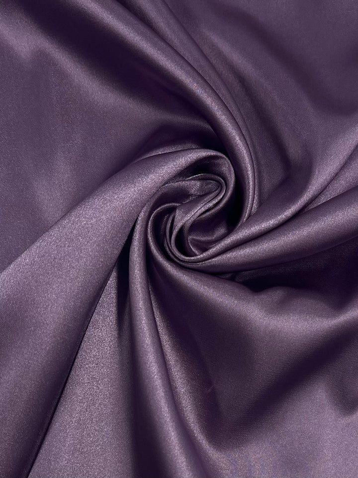 A close-up of Satin - Very Grape - 150cm from Super Cheap Fabrics, featuring smooth, shiny purple folds twisted into a spiral—highlighting the elegant, silky texture of this lightweight fabric.