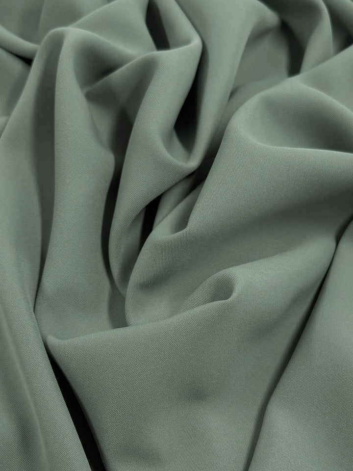 Super Cheap Fabrics' Microfibre Suiting in Dried Sage, 150cm wide, is smoothly textured and loosely draped, forming soft folds and gentle shadows.