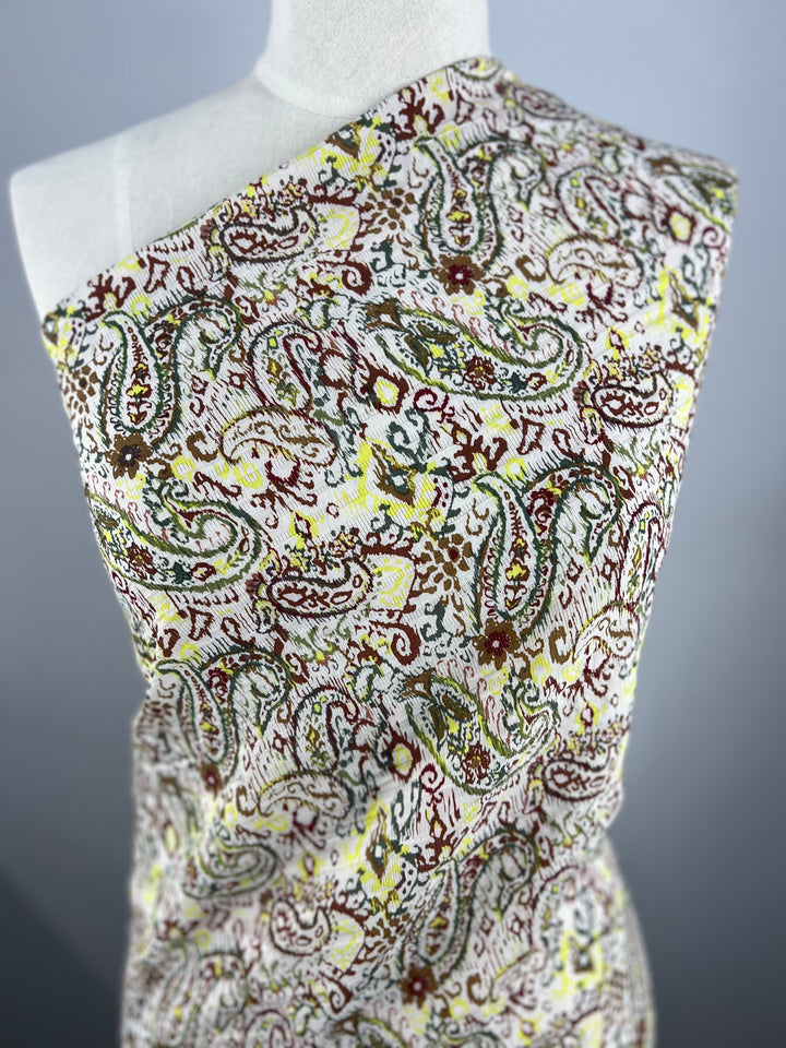 A mannequin is draped with the Voile - Paisley - 145cm by Super Cheap Fabrics, featuring green, yellow, and maroon intricate paisley on white. Ideal for warm weather clothing.